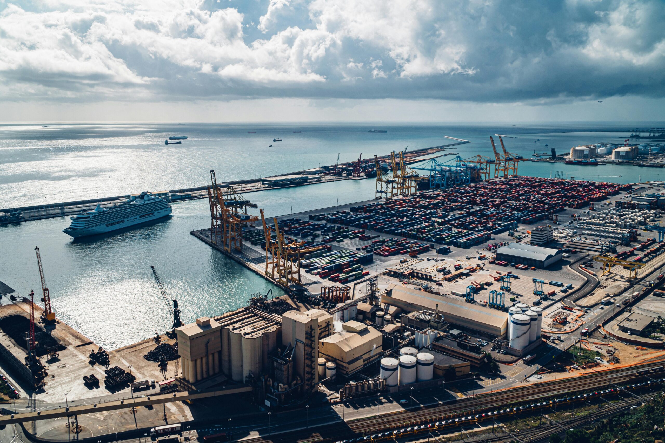 Aerial view of Barcelona port showcasing cargo containers, cranes, and cruise ship.